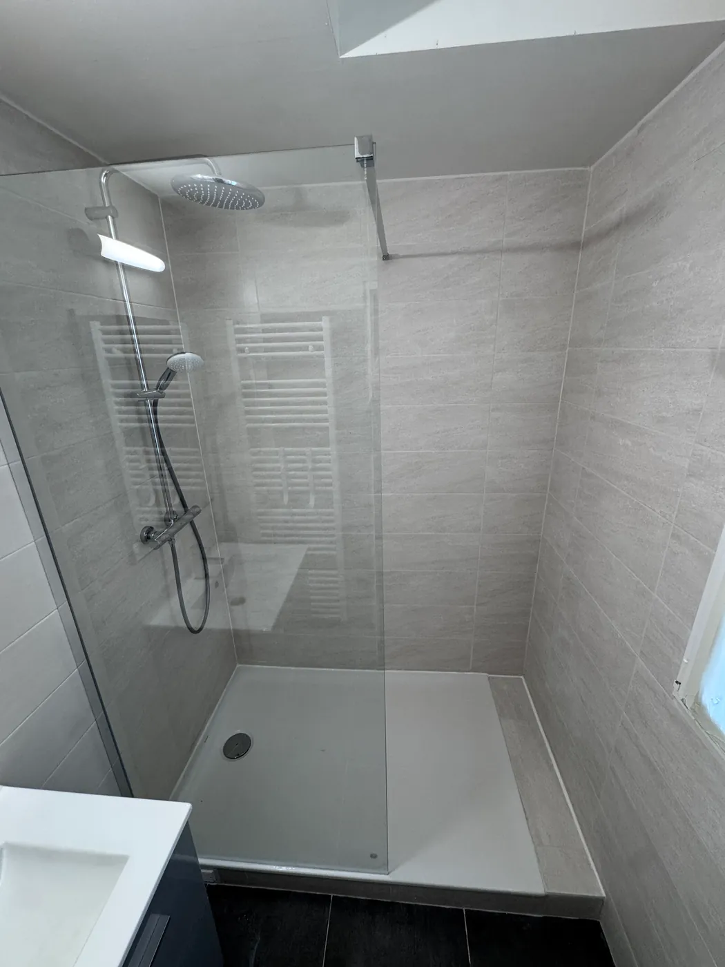 Douche à l'italienne carrelée grise avec paroi vitrée et sèche-serviettes