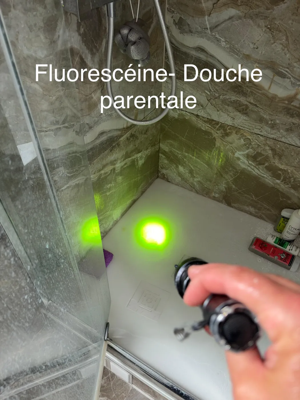 Traceur fluorescéine révélé à la lampe UV sur le receveur d'une douche parentale, annoté « Fluorescéine — Douche parentale »