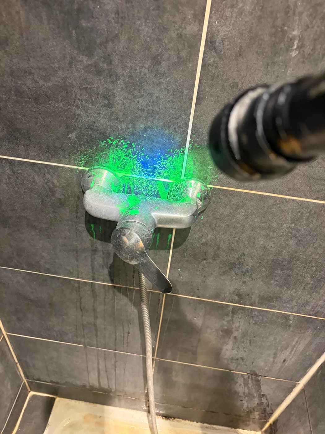 Mitigeur encastré dans un mur carrelé, traceur fluorescent révélé à la lampe UV autour du corps d'encastrement