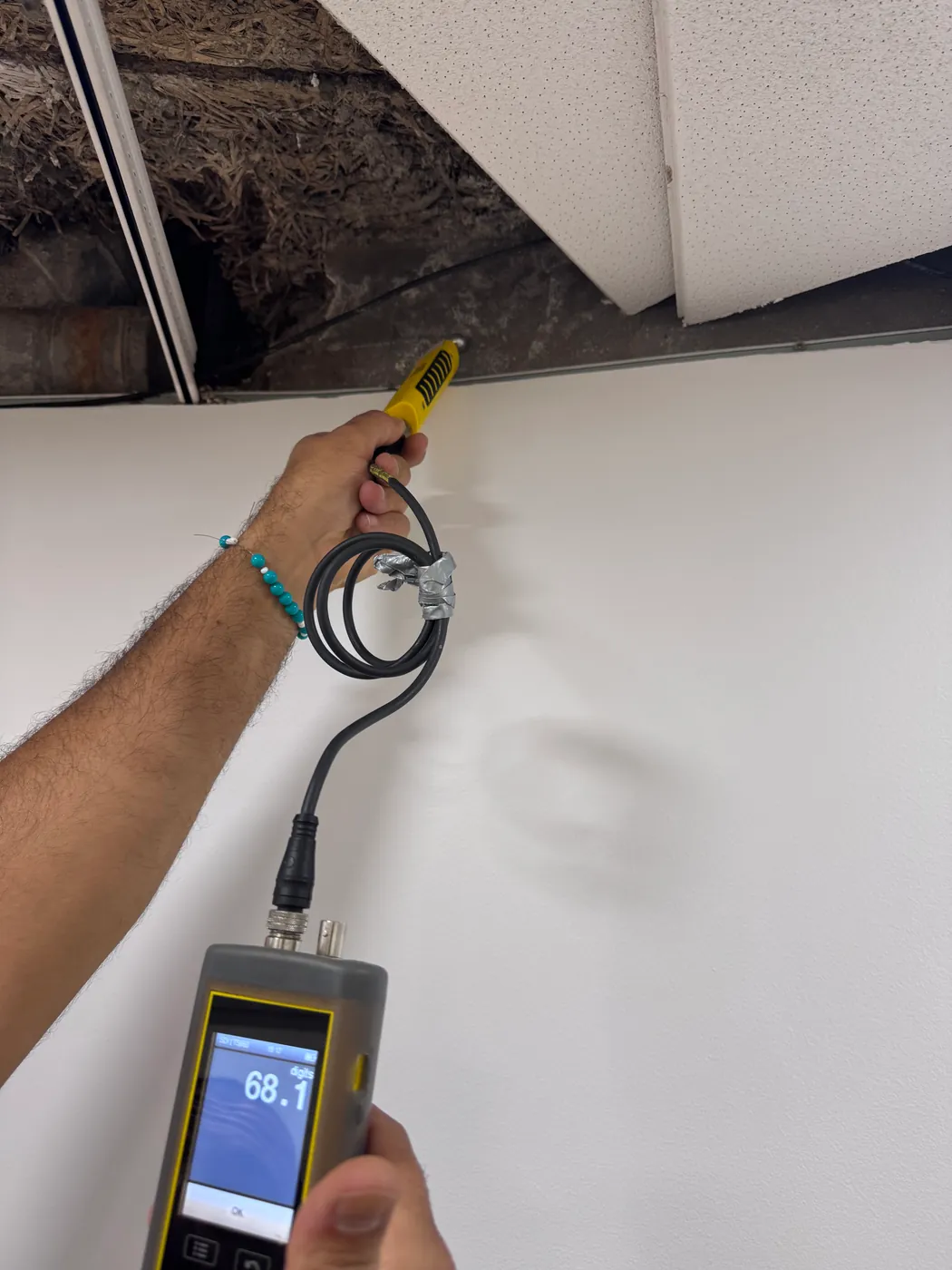 Humidimètre affichant 68,1 lors d'une mesure d'humidité sur un mur, sous un faux plafond ouvert