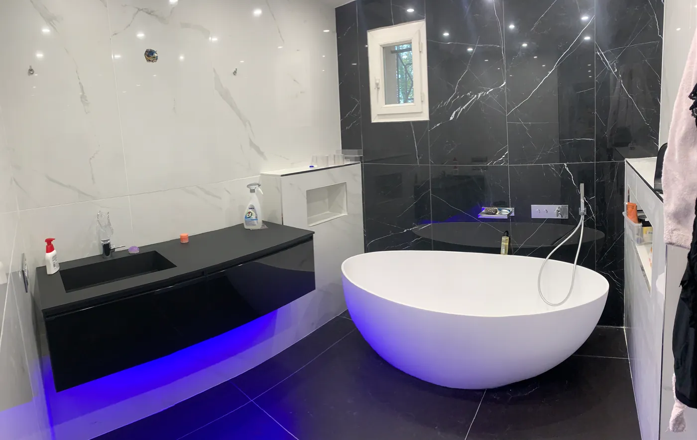 Salle de bain en marbre noir avec baignoire îlot rétroéclairée et plan vasque suspendu