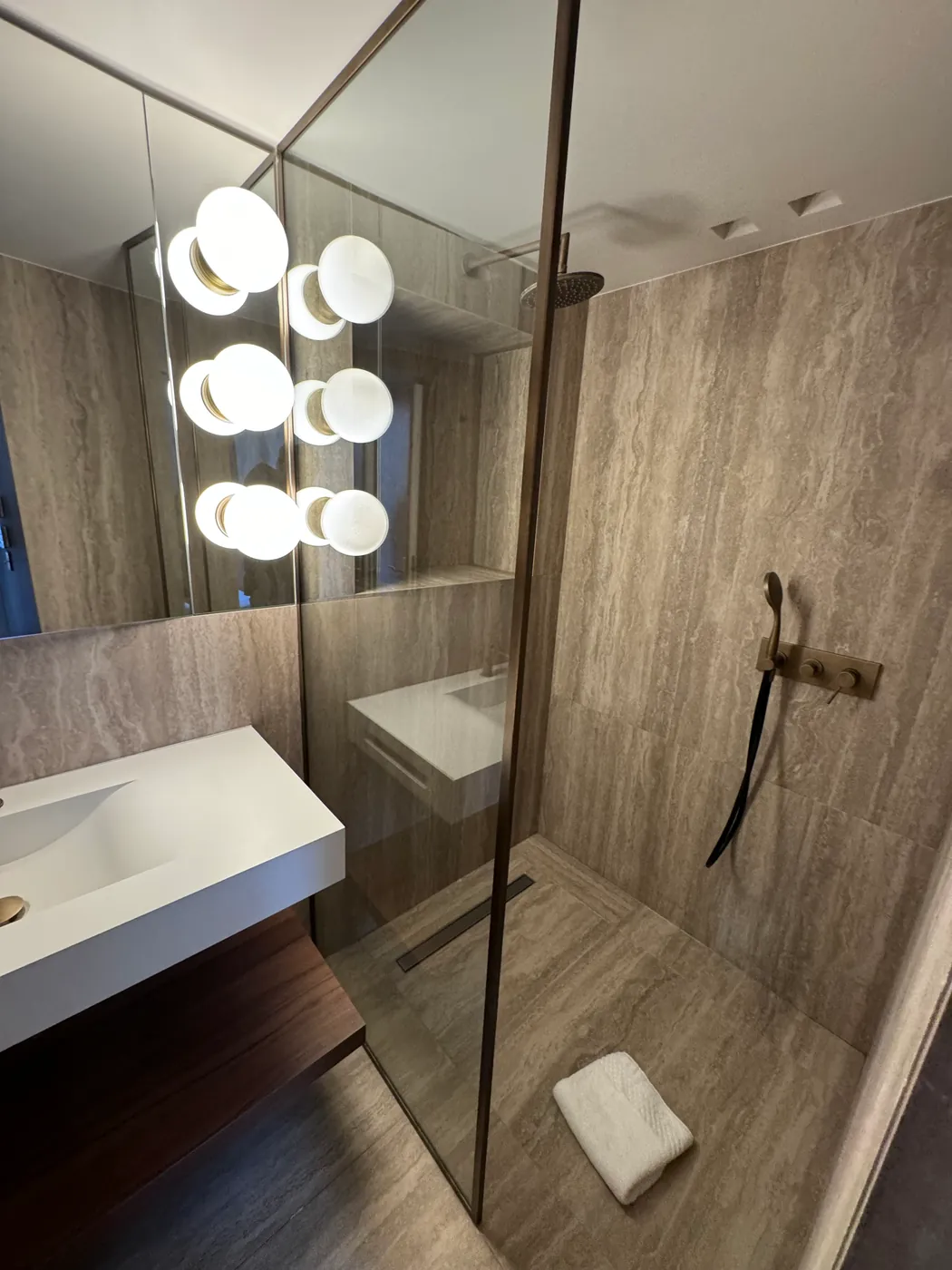 Salle de bain en travertin avec robinetterie dorée encastrée et douche à l'italienne