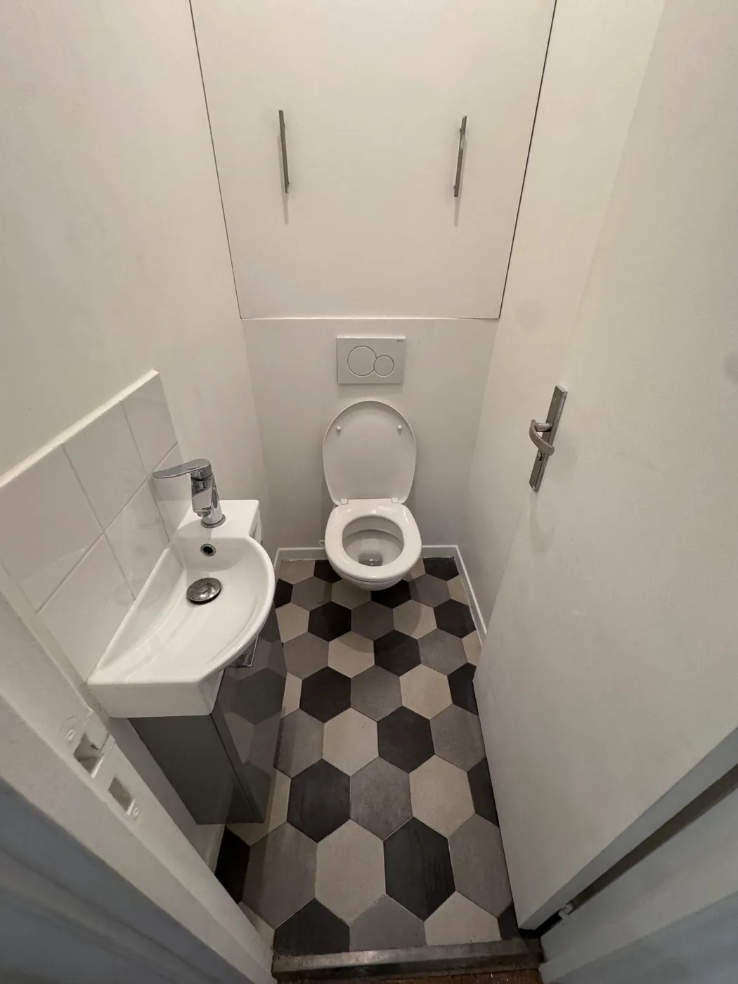 WC avec lave-mains d'angle et sol en carrelage hexagonal noir et blanc