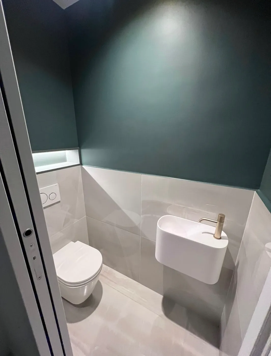 WC suspendu avec plaque de commande encastrée sur mur vert et faïence marbrée